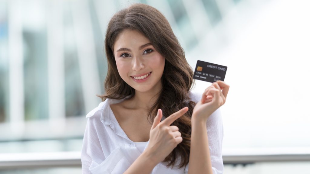 Smiling woman confidently showing a credit card – financial success or approval concept.