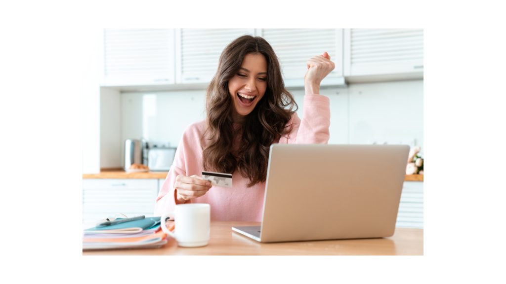 Excited woman using laptop with credit card in hand – online approval or purchase success.
