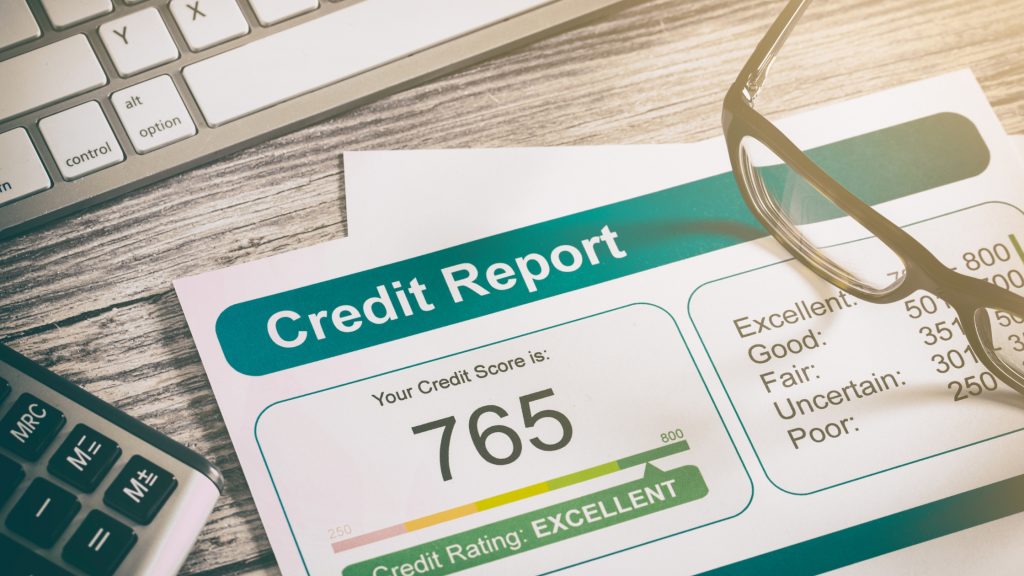 Credit report with 765 score marked as excellent, shown beside glasses and keyboard.