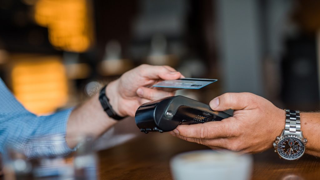 Customer making contactless payment with credit card using POS terminal at a cafe.