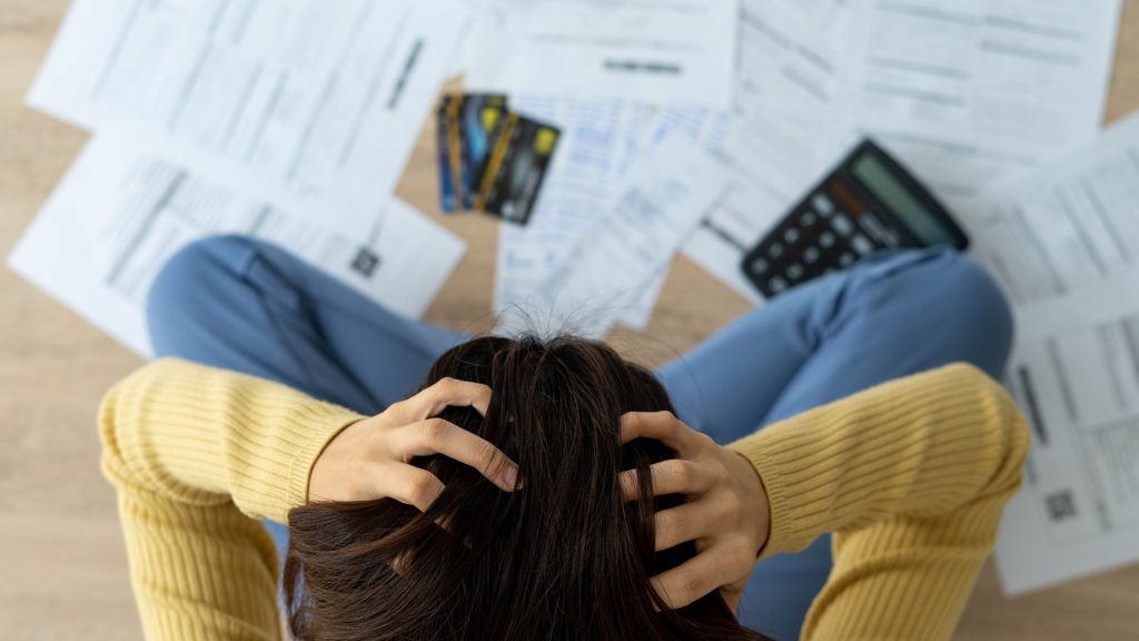 Overwhelmed person surrounded by credit card bills, debt notices, and a calculator.