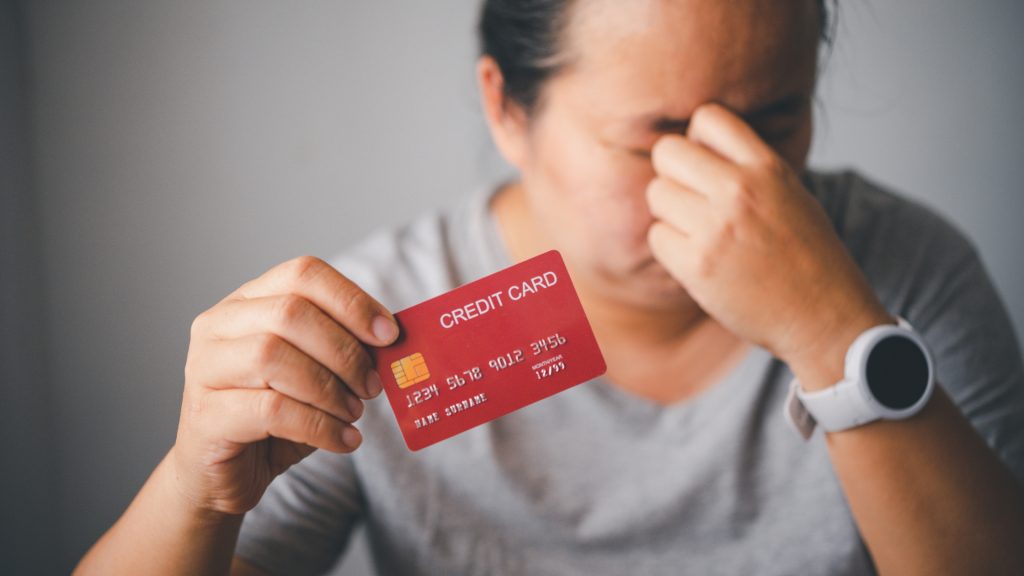 Stressed woman holding a credit card, symbolizing debt anxiety or financial hardship.