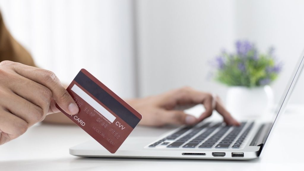 Close-up of hand holding a credit card while typing on a laptop for online payment or financial transaction