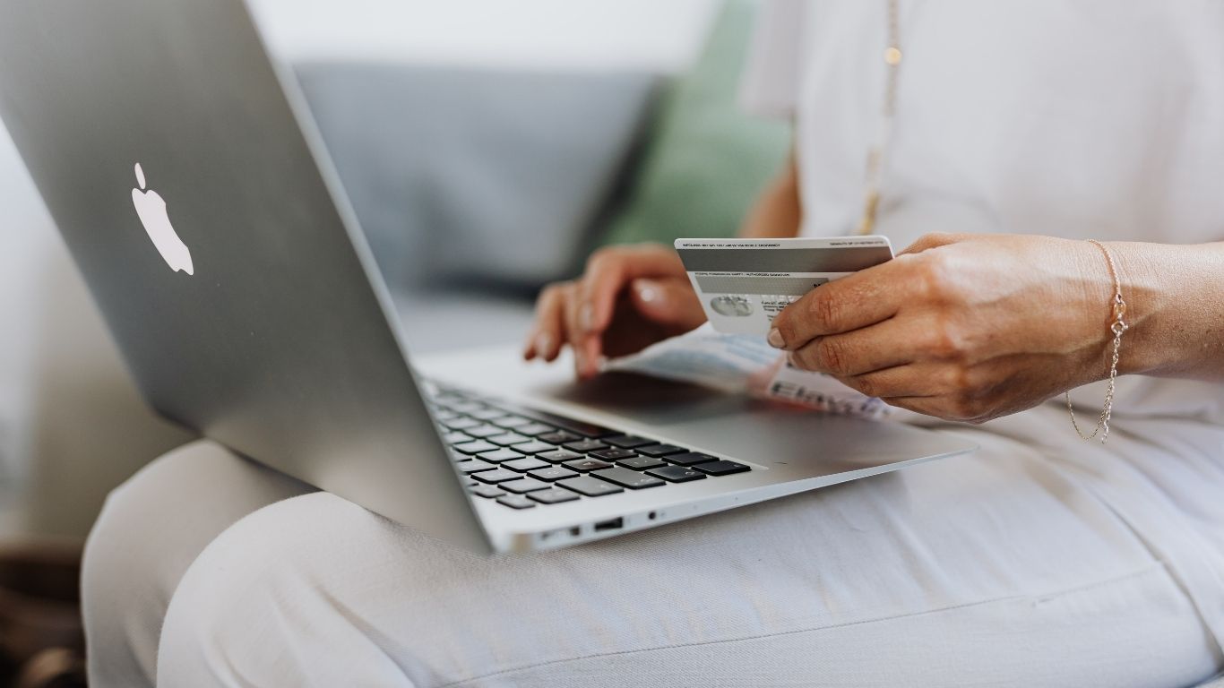 Close-up of person holding a credit card and typing on a MacBook laptop for an online transaction