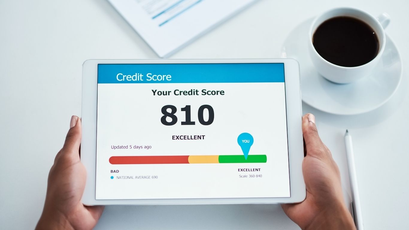 Person holding a tablet displaying an excellent credit score of 810 next to a cup of coffee
