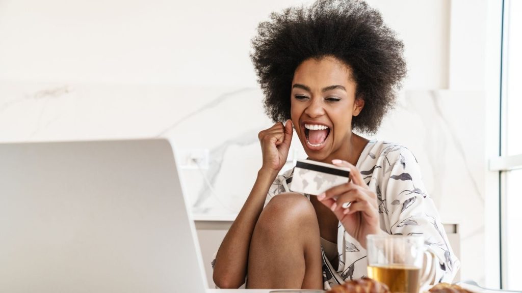 Excited woman holding a credit card while shopping online from home using a laptop