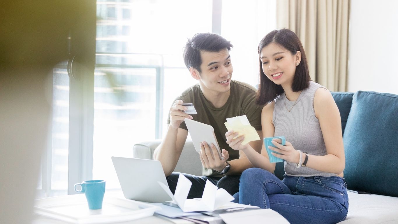 Young couple sitting on a couch reviewing credit card and financial documents together at home