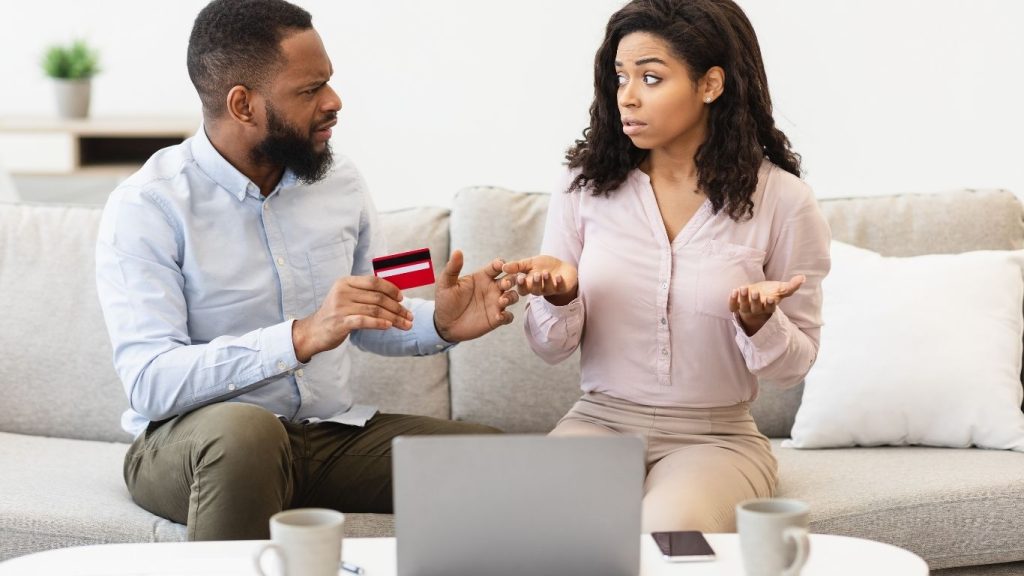 A frustrated couple discussing credit card debt at home with a laptop in front of them. Credit Repair After Loan Rejection.