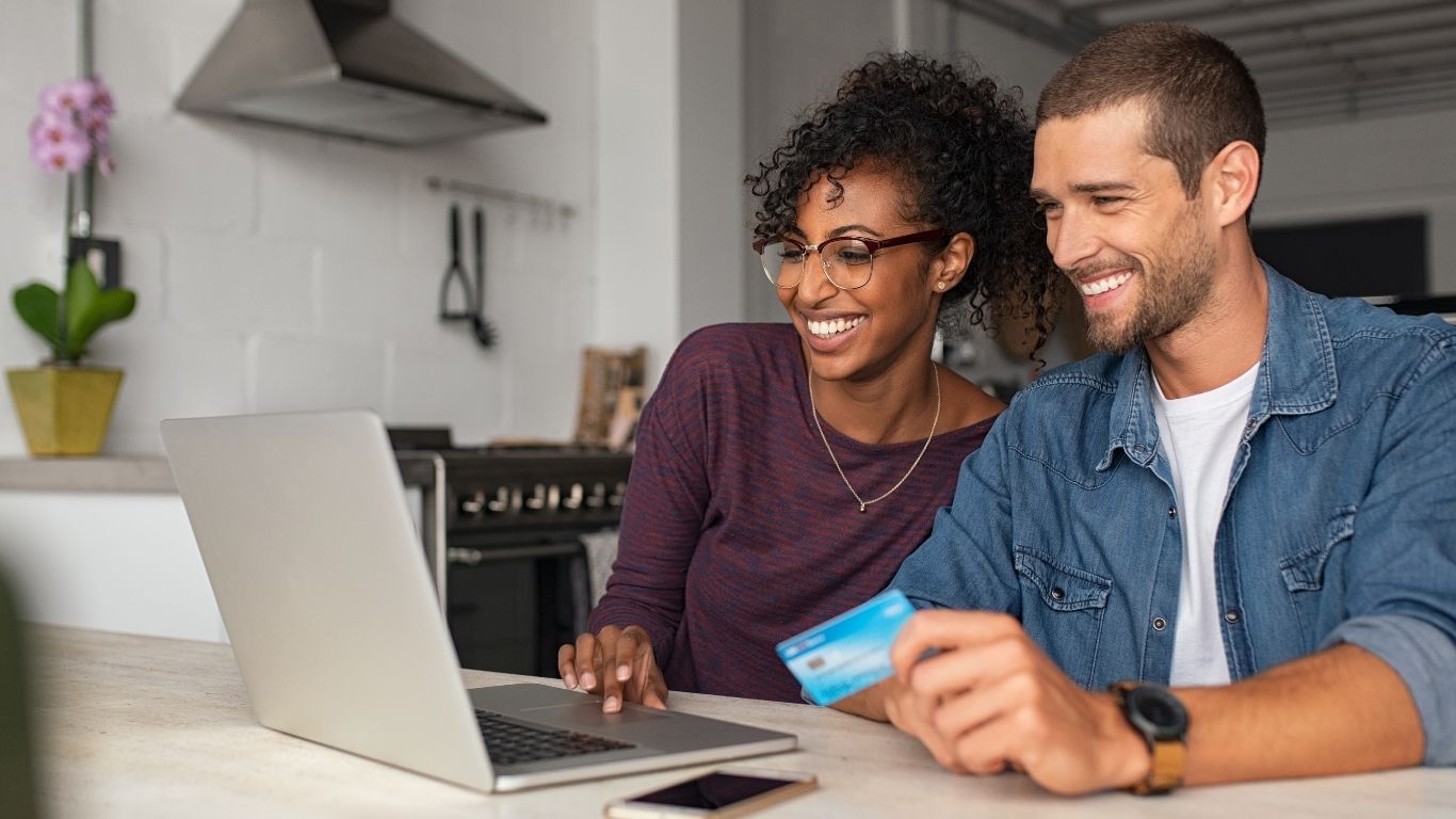 Happy couple using a laptop and holding a credit card while shopping online at home