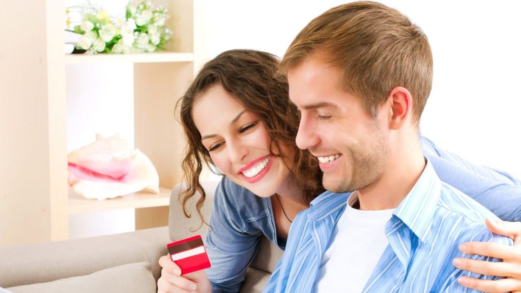 A smile. A Couple sitting on a couch holding a credit card and looking happy at home. Protect credit from debt collectors.