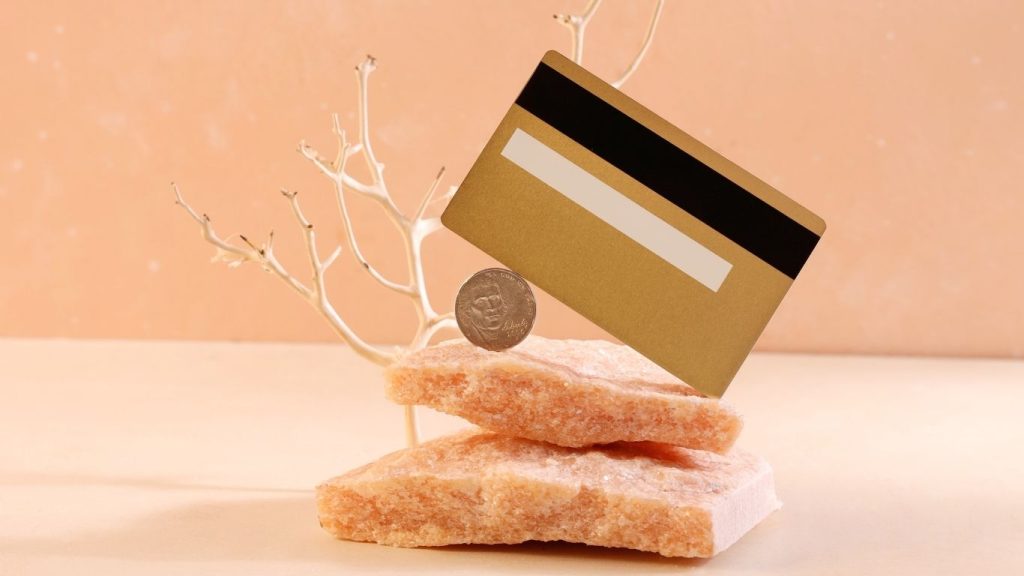 A gold credit card balanced on stacked salt rocks with a coin, symbolising financial balance and credit stability.