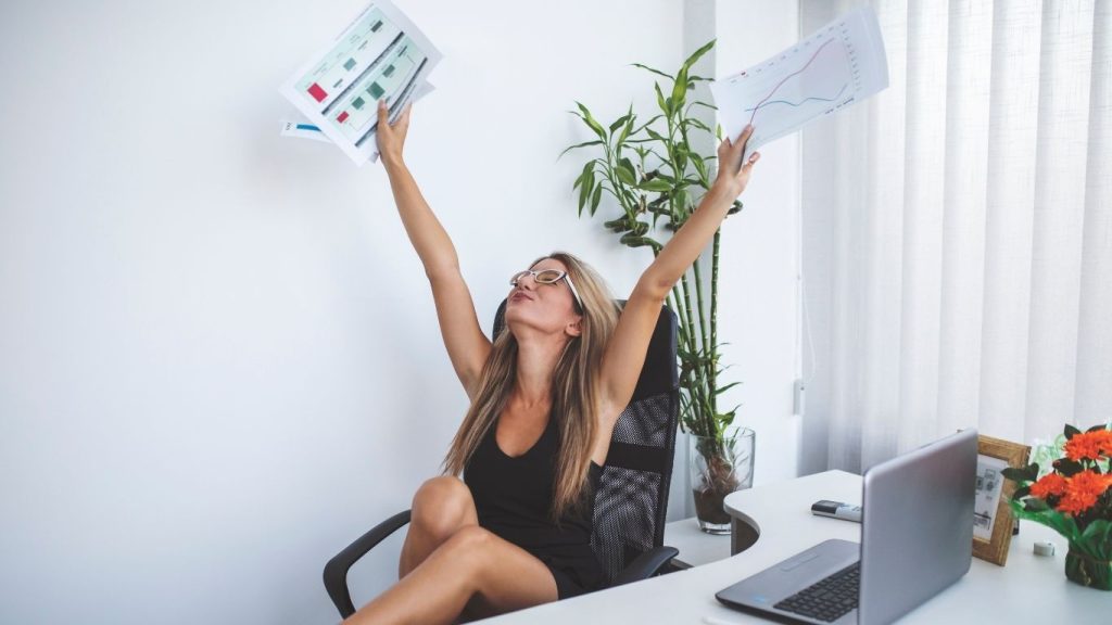 Excited woman celebrating financial success while holding documents in an office environment.
