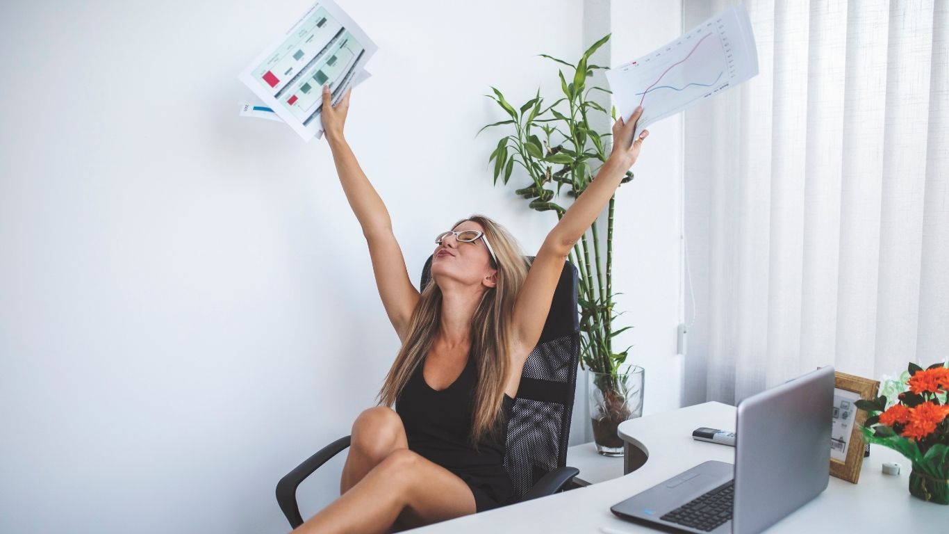 Excited woman celebrating financial success while holding documents in an office environment.