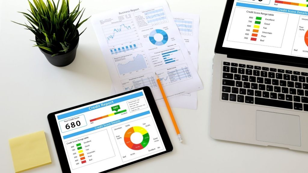 Credit report and score analysis on digital devices and printed charts, showing financial data visualization on a tablet and a laptop in a modern workspace.Rebuild credit before reapplying.