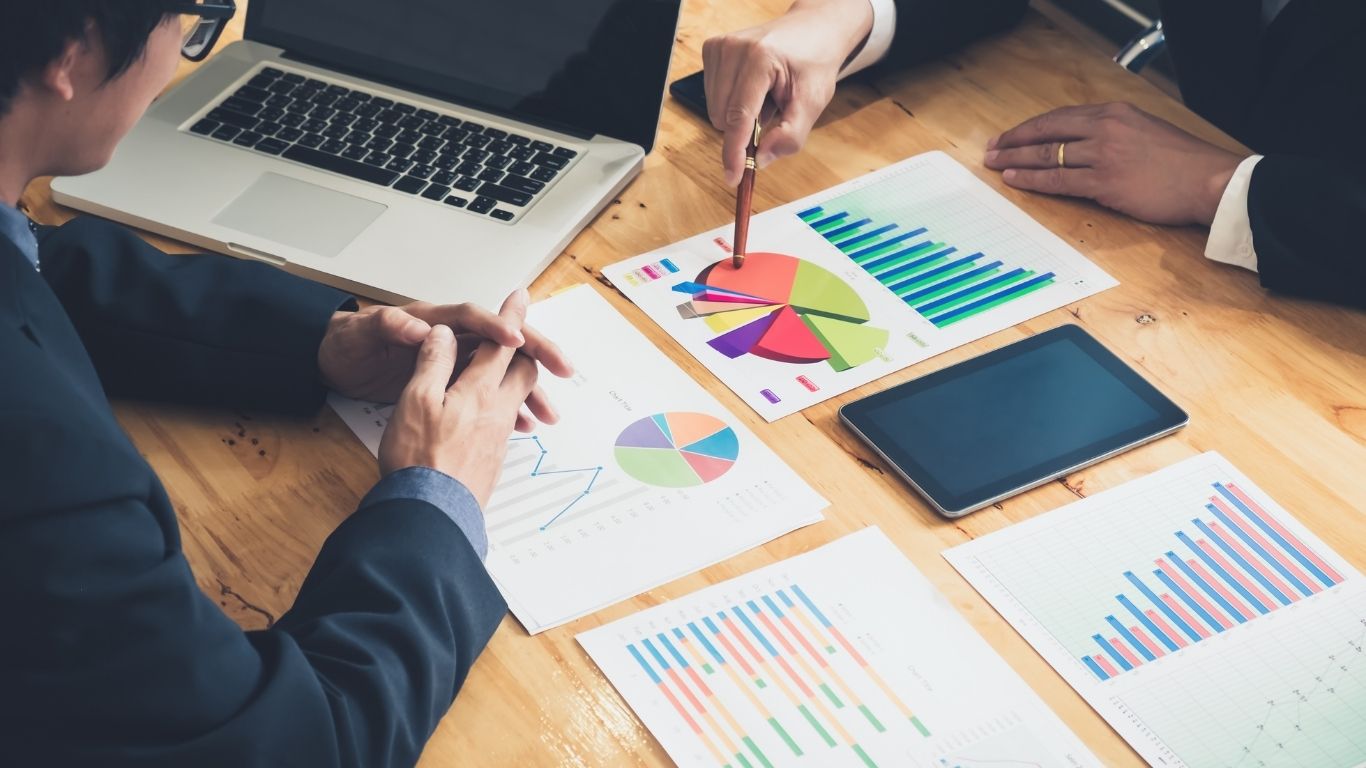 Business team analyzing financial graphs and charts during a data-driven marketing strategy meeting, with a laptop and tablet on the desk.