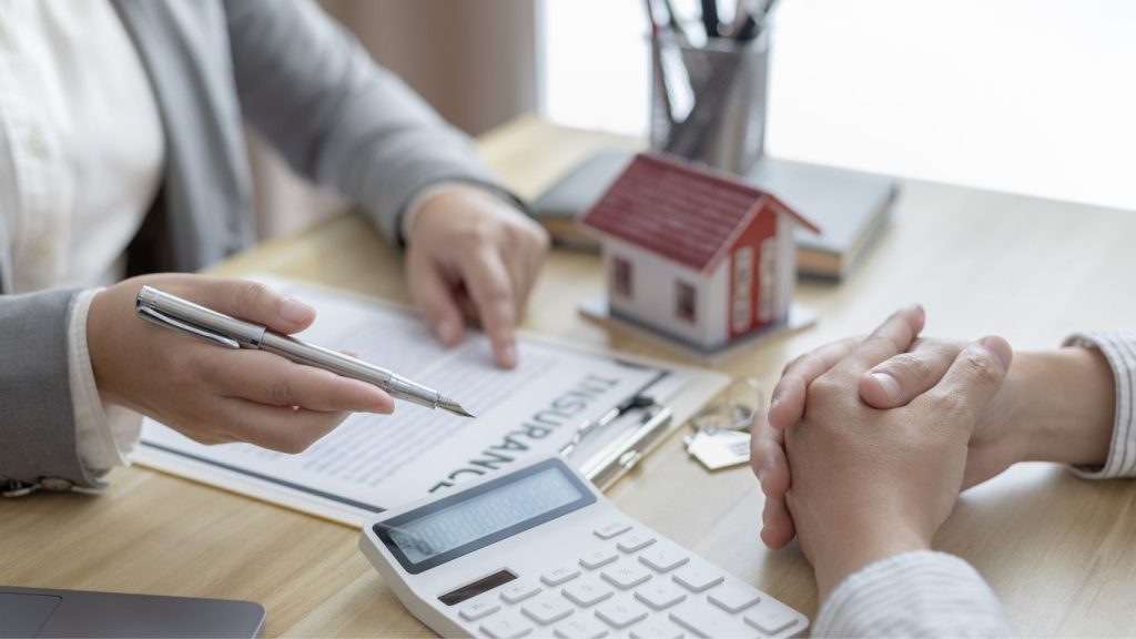 Two people discussing mortgage terms at a desk with calculator, keys, and house model