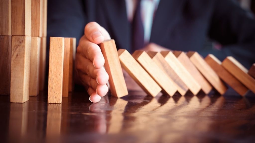 A businessman's hand stops a row of falling dominoes, symbolizing risk management or problem prevention.
