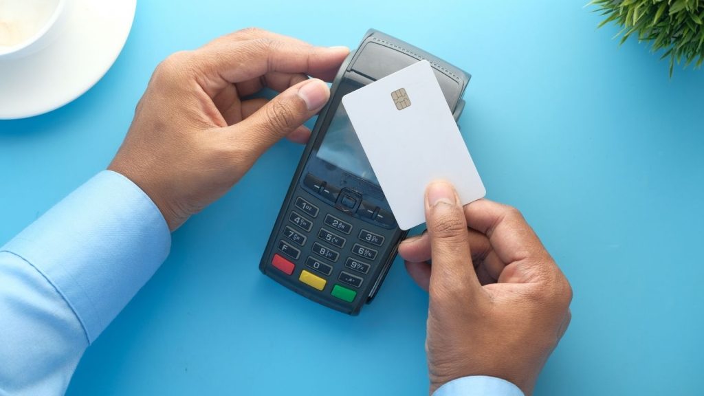 Contactless payment with white credit card over a POS terminal on blue background