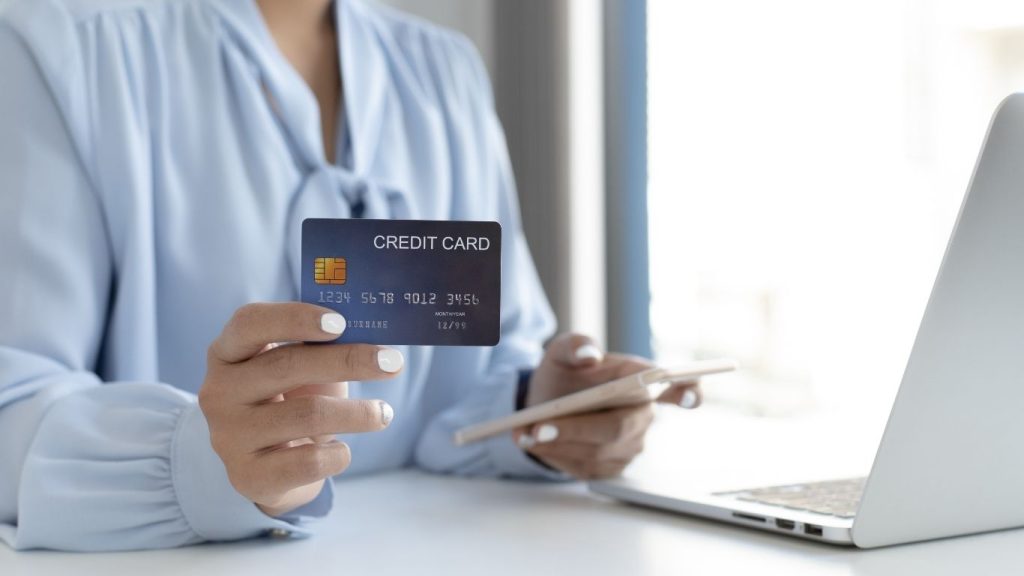 Person holding a credit card while using a laptop, indicating online shopping or payment.