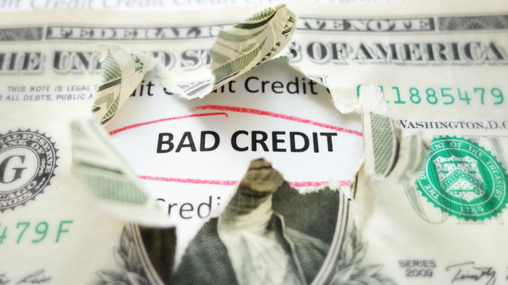 Bad credit text revealed under torn dollar bill, symbolizing financial stress and poor credit score.